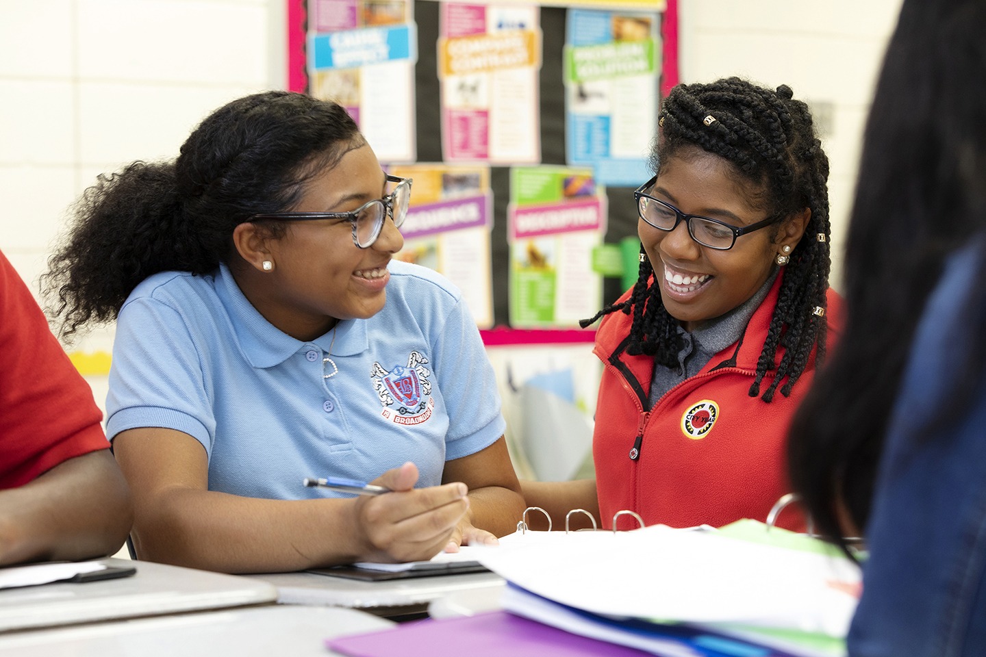 a student smiles and looks at an AmeriCorps member as they sit together at a table doing work