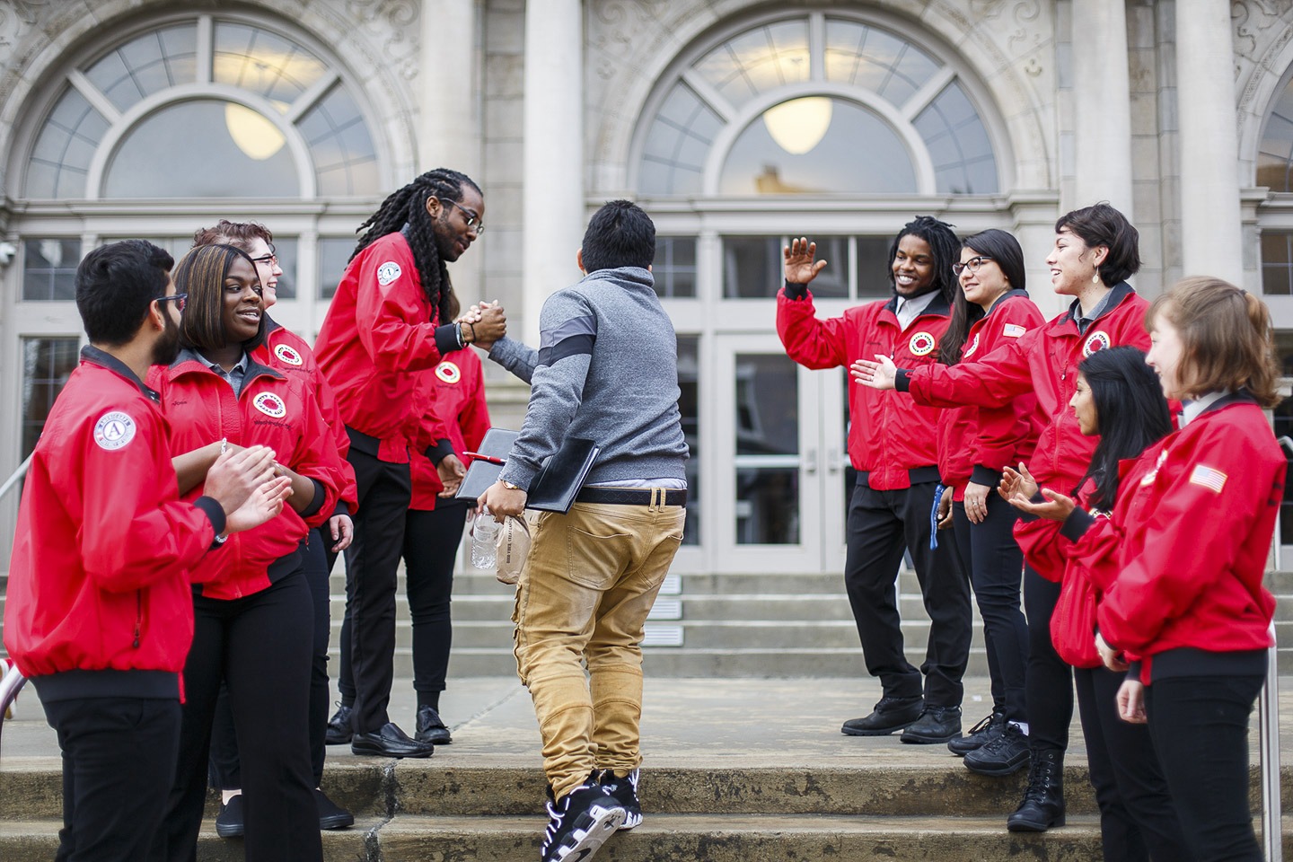 A group of AmeriCorps members line up outside of school to greet students with high-fives.