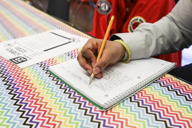 A student writes down notes with a pencil in a notebook.