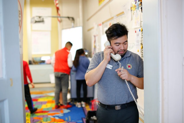 a city year americorps member on the phone while other americorps members and students are in the background in a classroom