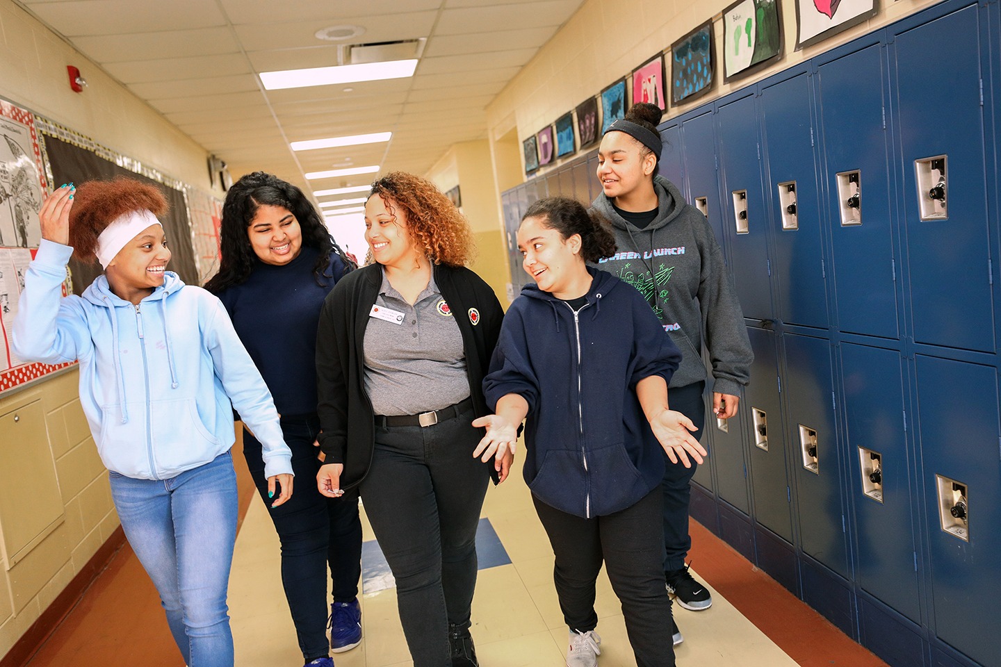 a city year americorps member walking with students in a hallway next to lockers