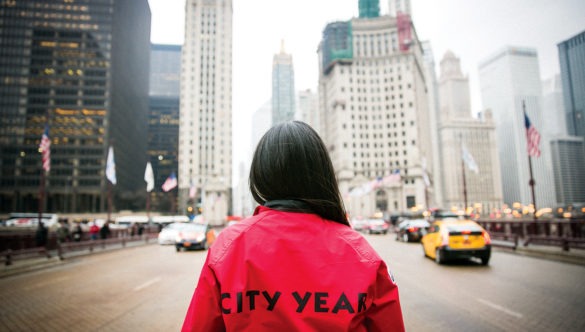 AmeriCorps member stands on a busy street looking up at the city.
