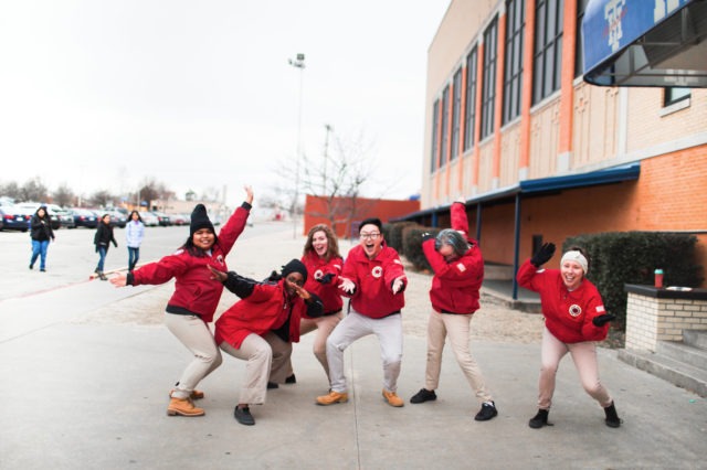 Six AmeriCorps members strike an energetic pose in front of a school
