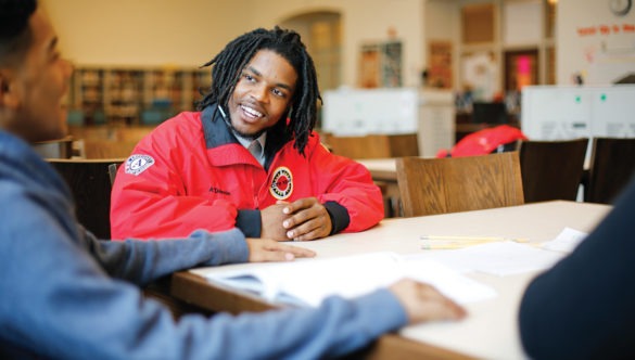 an americorps member sits at a table smiling at a student